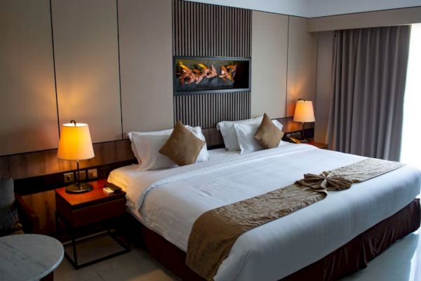 This image shows a neatly arranged bedroom with a large bed, two lamps on side tables, a wall-mounted decor piece, and a window with curtains.