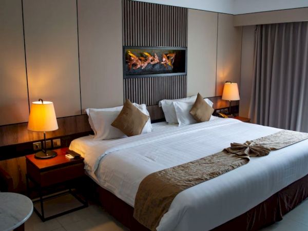 This image shows a neatly arranged bedroom with a large bed, two lamps on side tables, a wall-mounted decor piece, and a window with curtains.