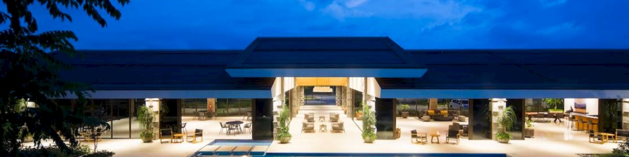 A luxurious outdoor pool area with an illuminated building, trees, and a clear evening sky in the background.