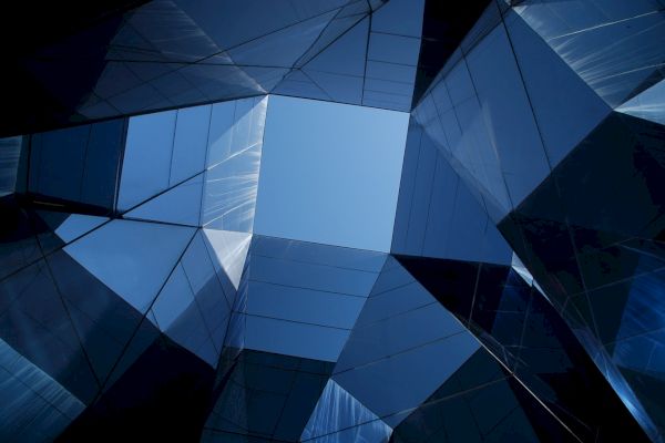 The image shows a geometric view of modern glass buildings, with their reflective surfaces creating an intricate, abstract pattern against the sky above.