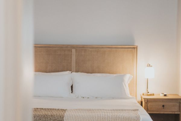 A cozy bedroom with a neatly made bed, a wooden headboard, a side table with a lamp, and a bench at the foot of the bed.