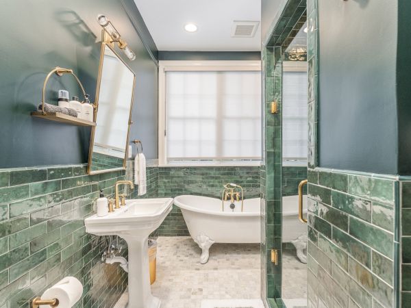 A bathroom with green subway tiles, a freestanding bathtub, a pedestal sink, a mirror, and gold fixtures, all creating a stylish look.