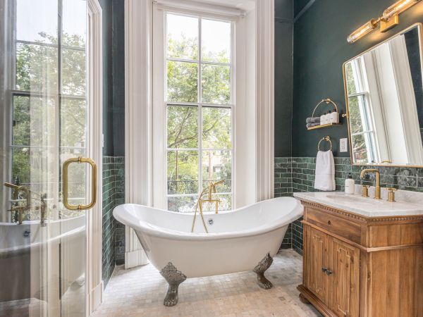 The image shows a bathroom with a freestanding tub, large window, glass shower, wooden vanity, green subway tiles, and a mirrored wall.
