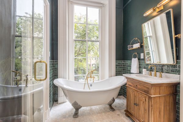 The image shows a bathroom with a freestanding tub, large window, glass shower, wooden vanity, green subway tiles, and a mirrored wall.