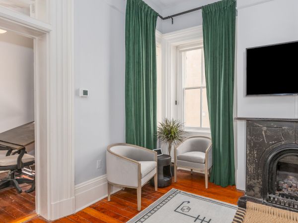 A room with two white chairs, green curtains, a wall-mounted TV, a fireplace, and a small table with a plant on it, next to a window, ends the sentence.