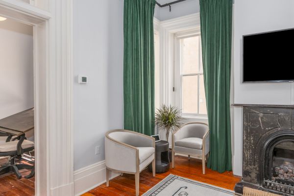 A room with two white chairs, green curtains, a wall-mounted TV, a fireplace, and a small table with a plant on it, next to a window, ends the sentence.