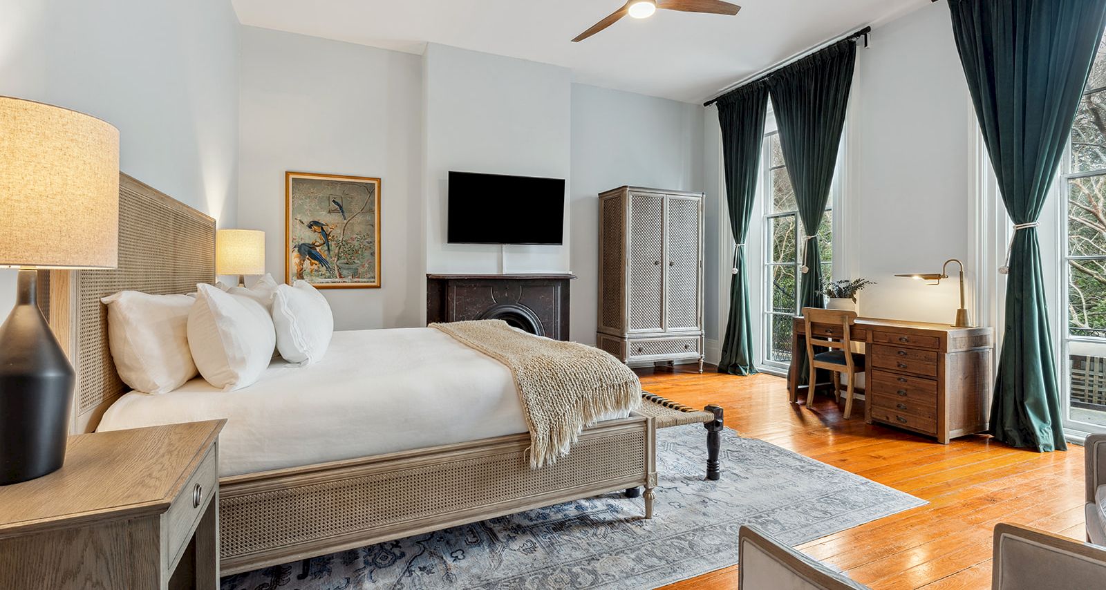 A stylish hotel room with a king bed, fireplace, flat-screen TV, desk, and large windows with dark curtains, plus a seating area and wooden floor.