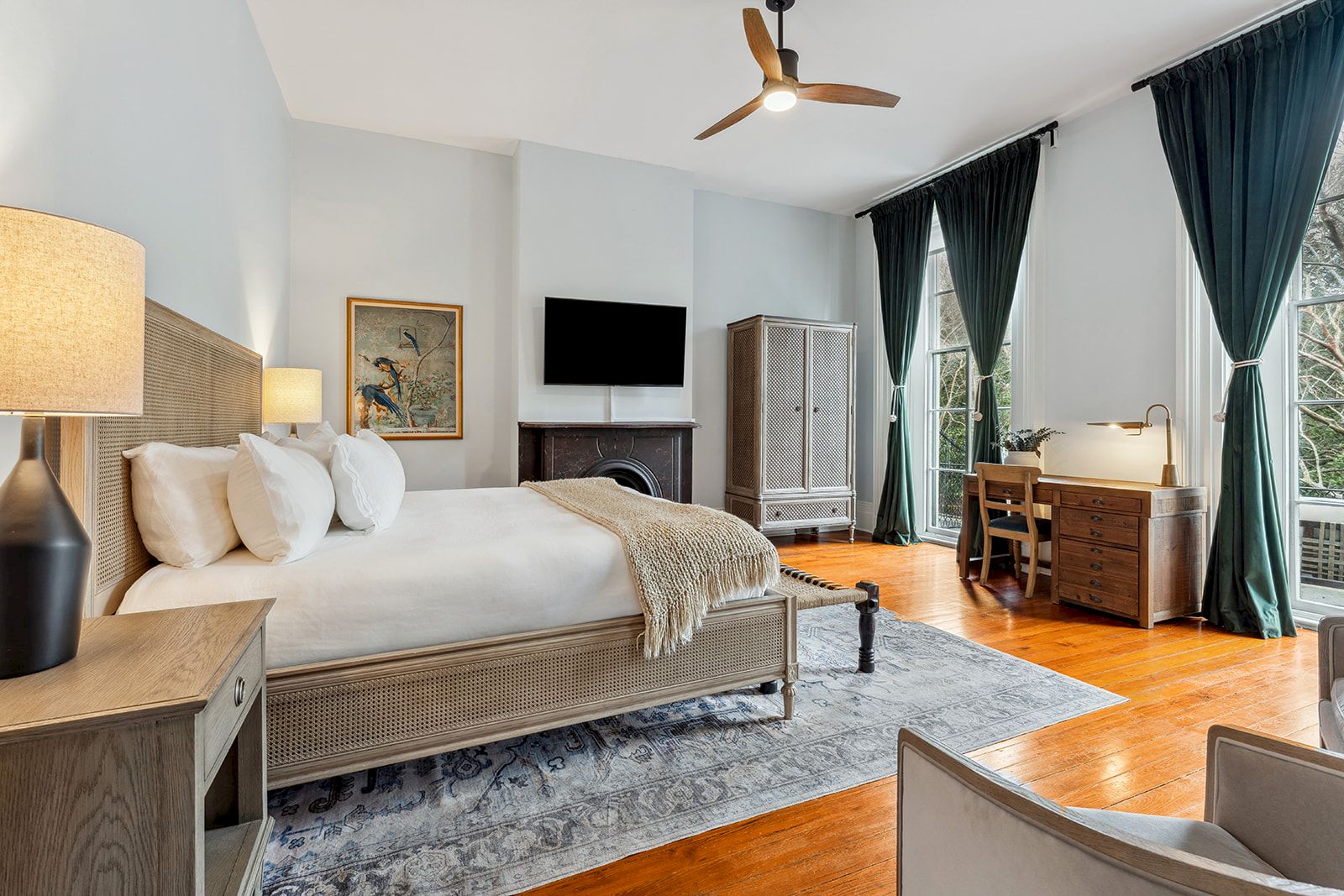 A stylish hotel room with a king bed, fireplace, flat-screen TV, desk, and large windows with dark curtains, plus a seating area and wooden floor.