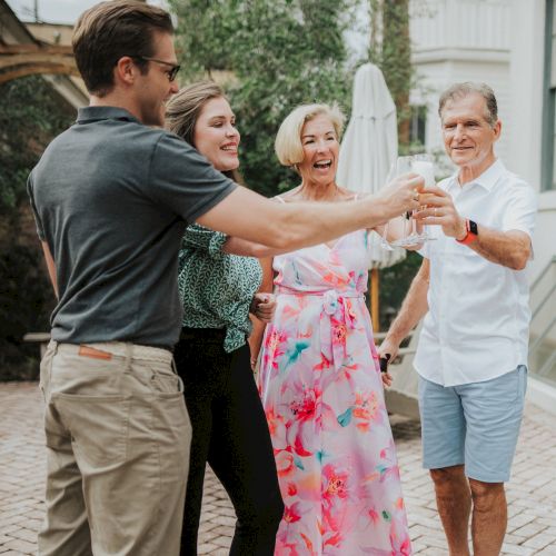 A group of four people is smiling and clinking glasses in a celebratory toast in a backyard setting.