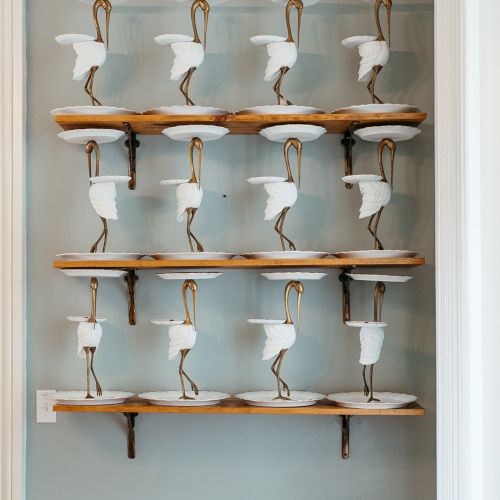 A wall-mounted wine rack with multiple copper pipes holding glass bottles, arranged on wooden shelves.