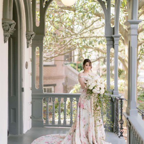 A woman in a light dress stands under an arched outdoor gazebo with greenery in the background.