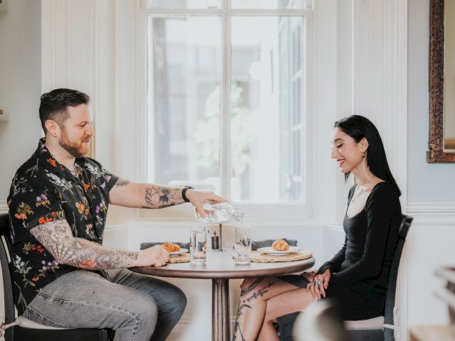 A couple sits at a table in a brightly lit room, enjoying pastries and coffee.