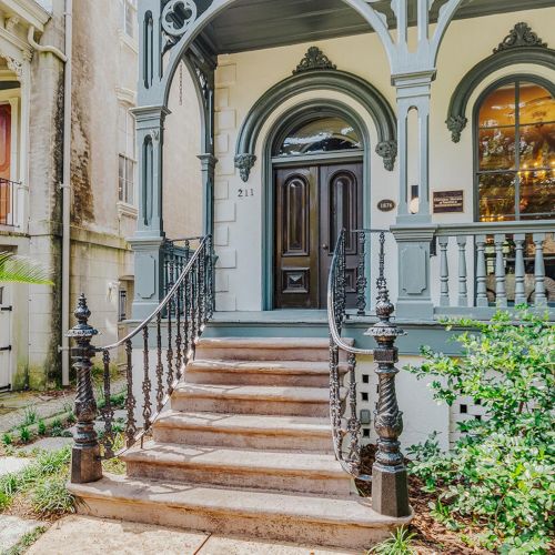 Colorful courtyard with arched doorways, potted plants, and a stone staircase leading to a blue door, tucked behind a charming fence.