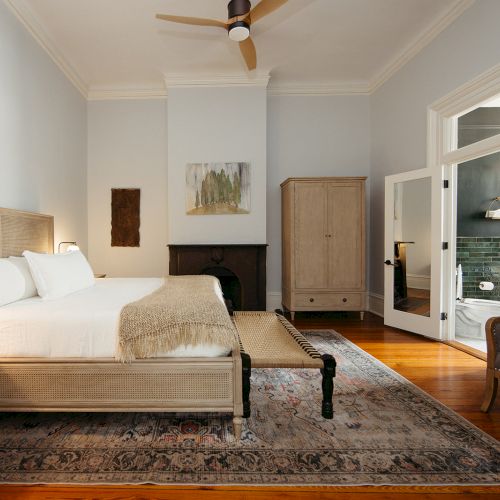 A bright, modern living room with a beige sofa, wooden coffee table, and a mounted TV; large windows with blinds let in natural light.