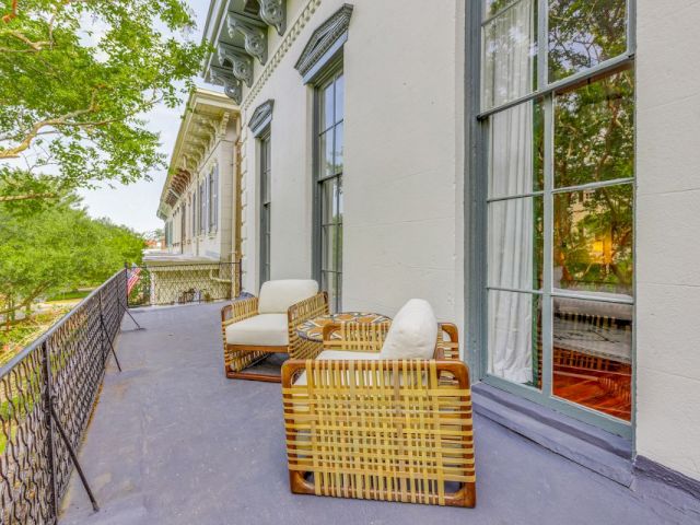 A balcony with wicker chairs and a railing overlooking a tree-lined area