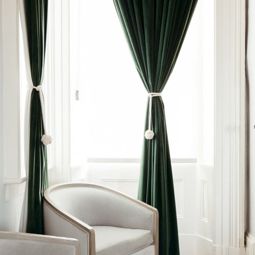 A chic corner with a light gray chair, dark green drapes, and white doors, framed by rich wood flooring.