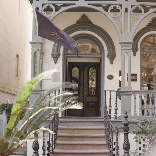 The image shows an ornate entrance to a building with decorative woodwork, a staircase with railings, a black door, and a flag hanging to the side.