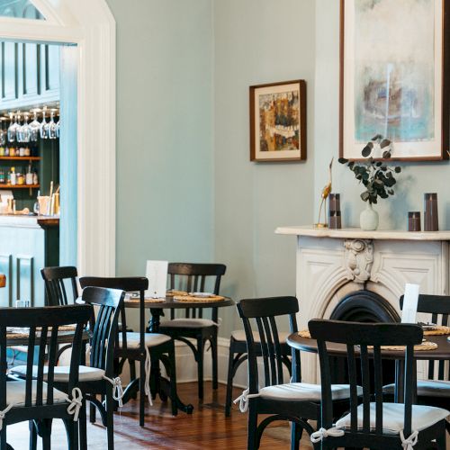 The image shows a cozy café interior with black chairs, wooden floor, a fireplace, and wall art. A bar with shelves is in the background.