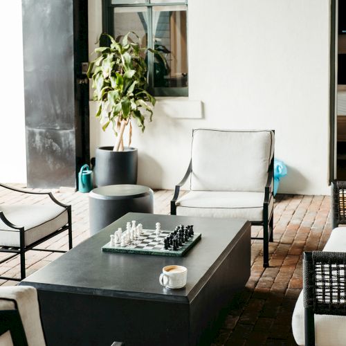 The image shows an outdoor seating area with armchairs, a coffee table with a chessboard and a cup, plus a plant in the background.