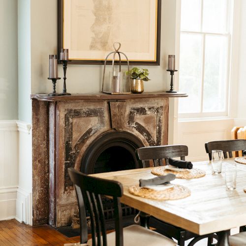 A cozy dining area features a wooden table, black chairs, a vintage fireplace with candles, decor, and a large framed map on the wall.