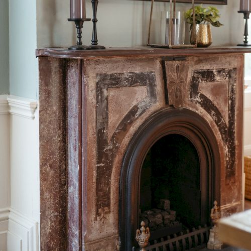 An ornate fireplace with candles and decorative items on the mantel, set against a light blue wall with white wainscoting.