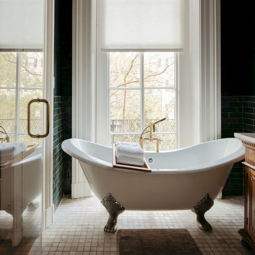 A luxurious bathroom features a clawfoot bathtub, large windows, wooden vanity, and elegant fixtures, creating a serene atmosphere.