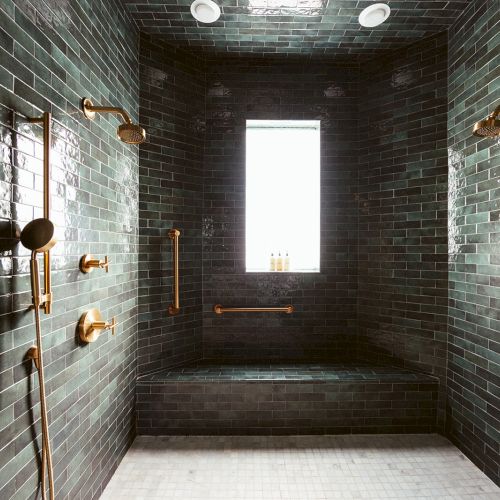 A luxurious shower room with dark green tiles, gold fixtures, a window, and a towel on the right.