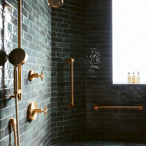 The image shows a modern shower with dark green tiles, gold fixtures, and a window with a ledge holding toiletries.