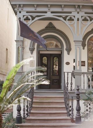 A grand hotel entrance with arched doorway, ornate porch railings, and a purple flag fluttering beside the steps.