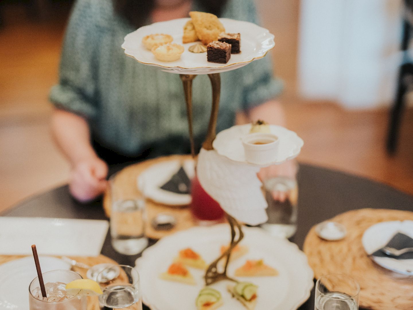 a tiered serving dish with pastries and brownie on a table with drinks