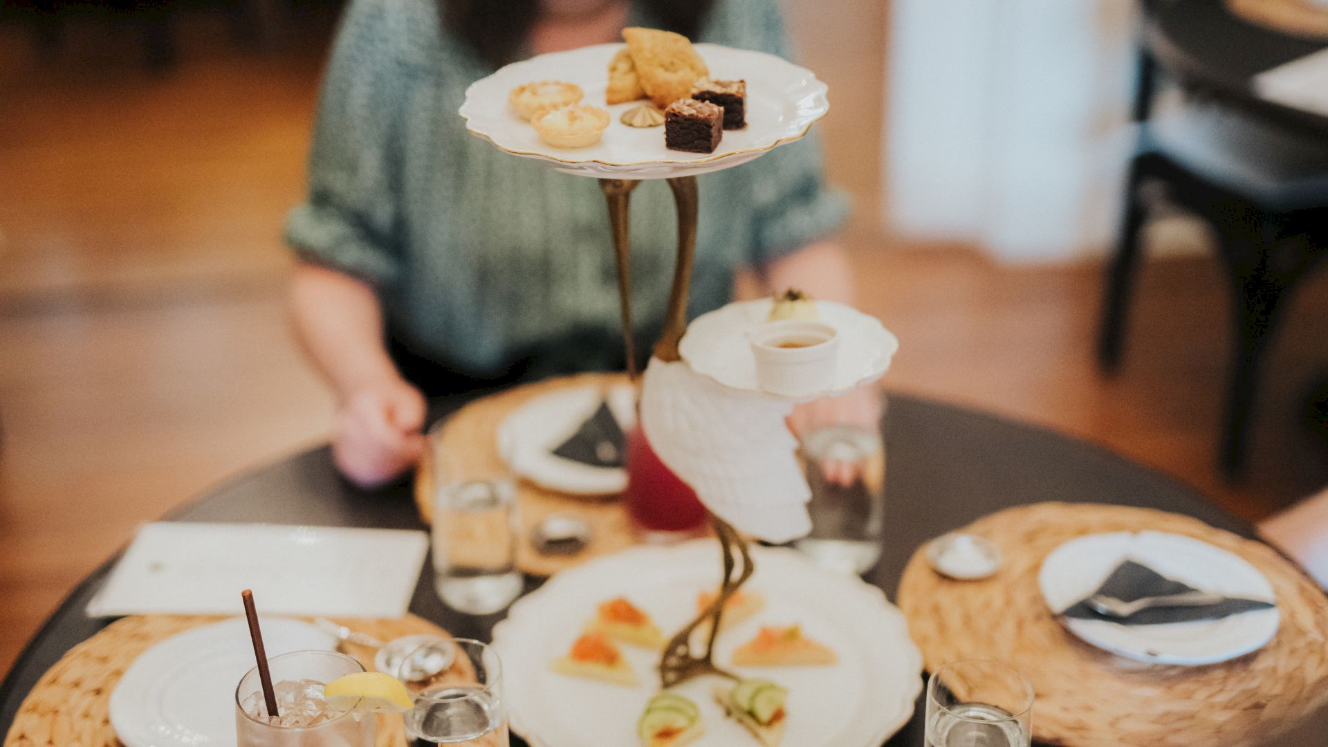 A table set for brunch with a tiered stand holding assorted pastries and brownies above friends&rsquo; plates.