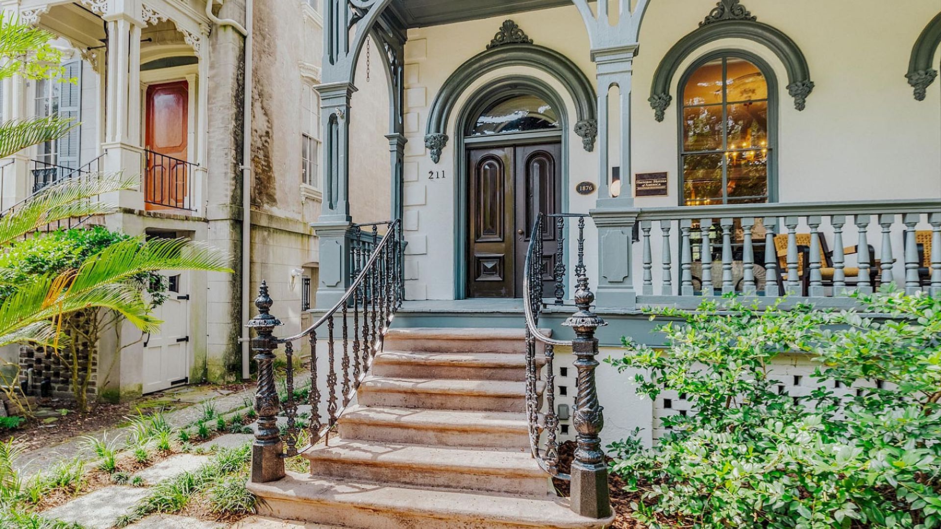 An elegant historic house entrance with arched doorways, wrought-iron railings, and steps leading to a front porch.