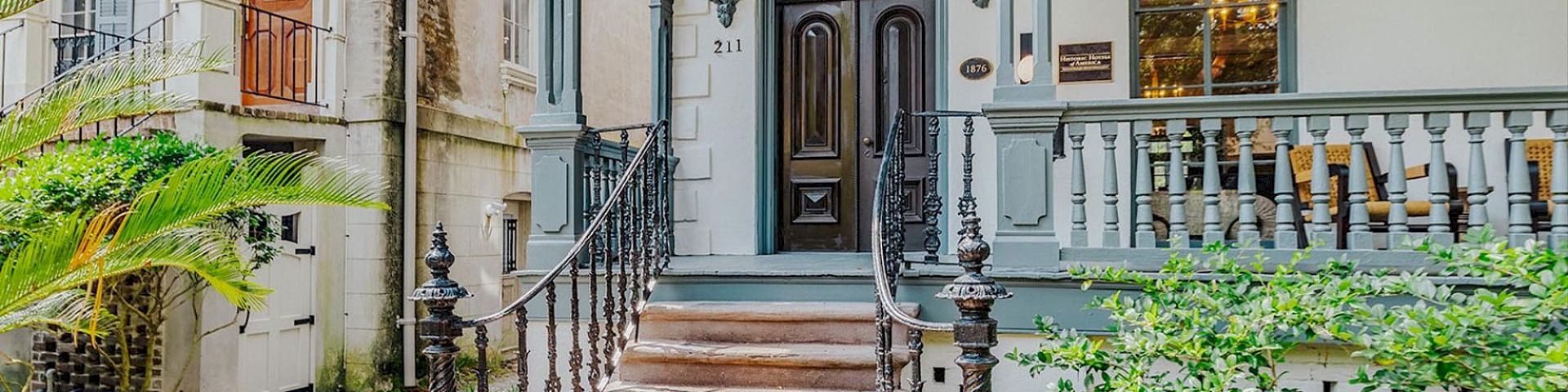 An elegant historic house entrance with arched doorways, wrought-iron railings, and steps leading to a front porch.