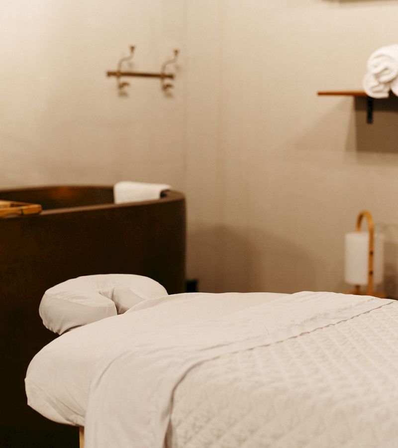 A massage table and tub in a spa room with white linens and towels.
