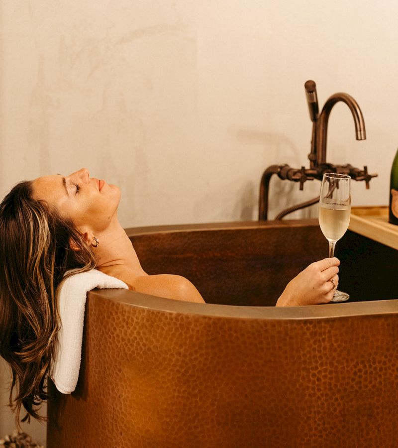 A woman relaxing in a copper bathtub with a glass of wine.