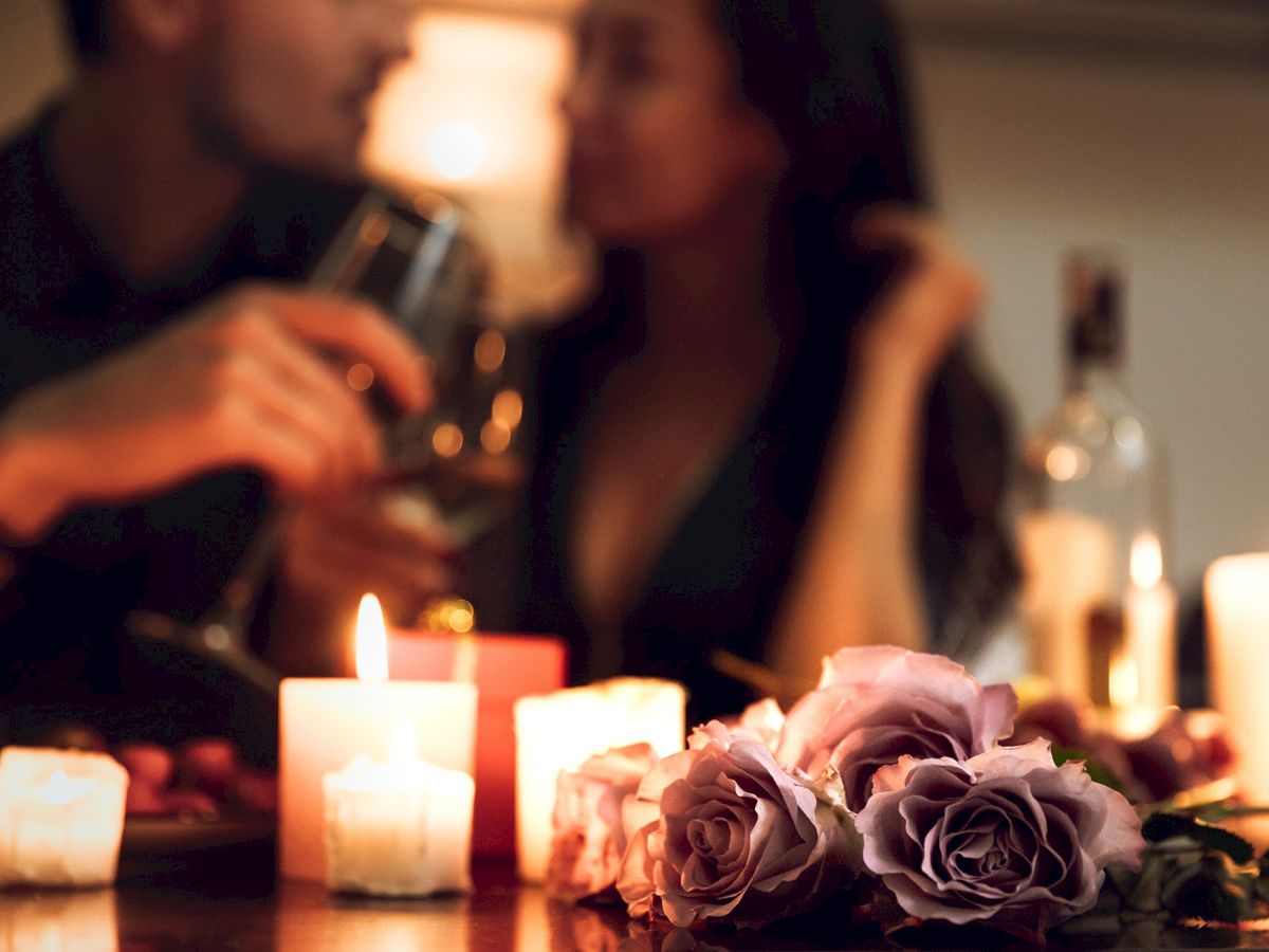 A romantic setting with candles, roses, and a couple holding glasses, creating an intimate ambiance.