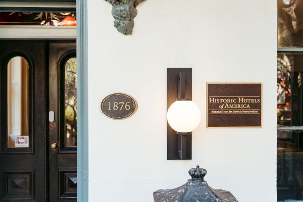 The image shows a building entrance with plaques for "1876" and "Historic Hotels of America," and a decorative outdoor light.