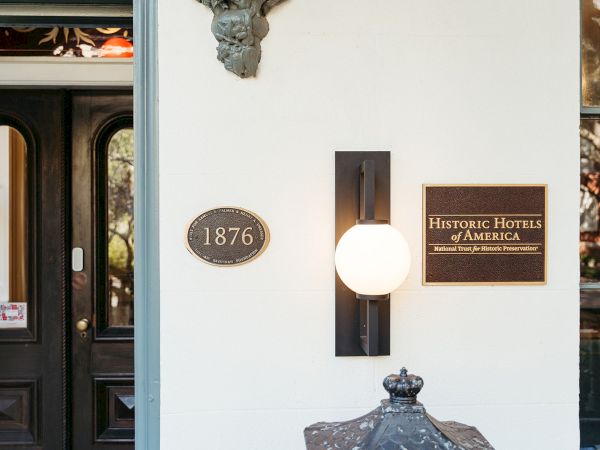 The image shows a building entrance with plaques for "1876" and "Historic Hotels of America," and a decorative outdoor light.