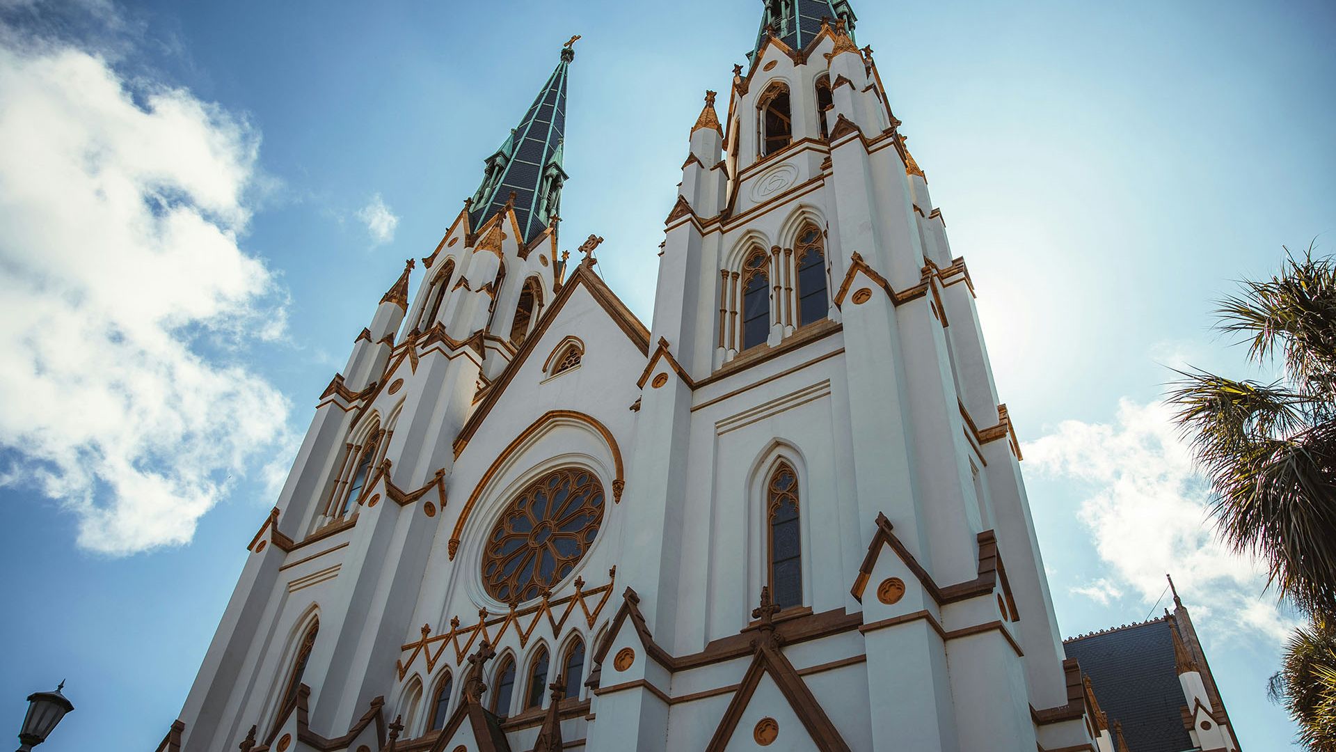 A grand white church with two tall green-trimmed steeples and ornate golden details against a bright blue sky.