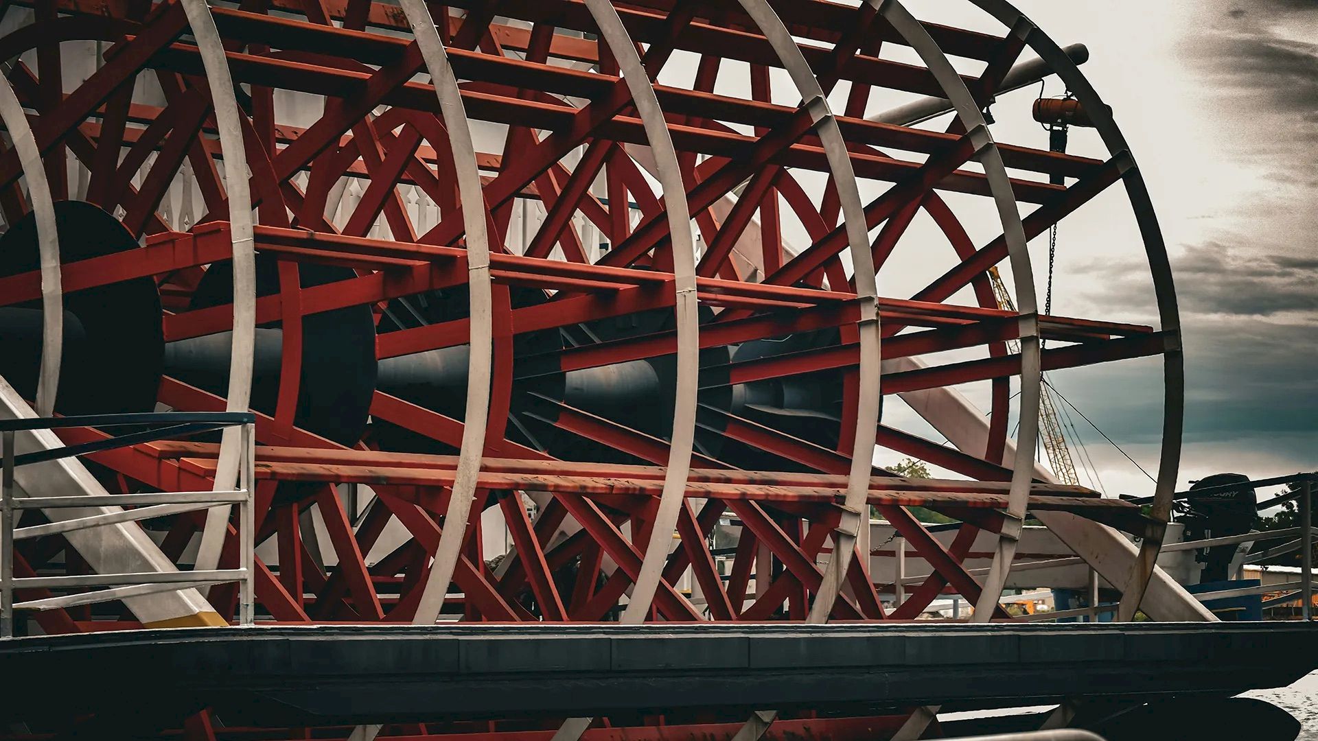 Industrial red-and-white spoked wheels along a dock, with rails and moored structures in a moody, cloudy scene.