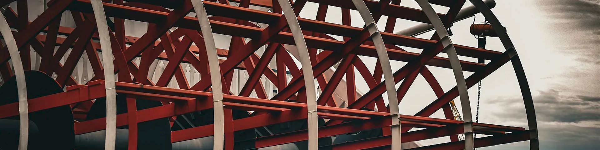 Industrial red-and-white spoked wheels along a dock, with rails and moored structures in a moody, cloudy scene.