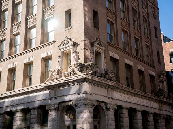 A stone-era building with ornate carved fa&ccedil;ade and arched windows, sunlit corner detailing, classic architectural style.