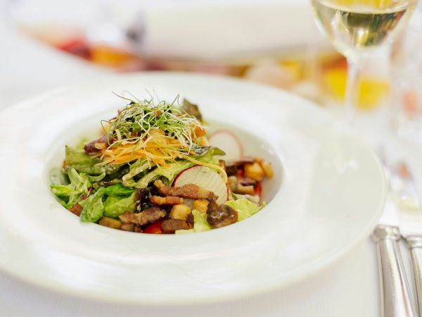 Delicious plated salad with greens, crispy toppings, roasted veggies, and delicate garnish, all presented in a chic white dish.