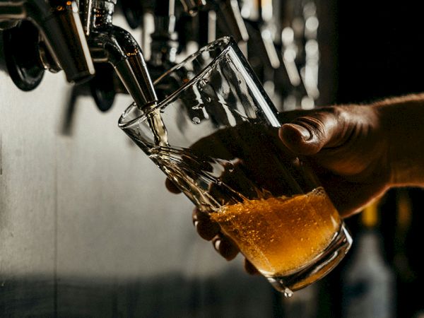 Pouring a glass of beer from a tap, with bubbles rising in the amber liquid as the glass tilts under a draft nozzle.