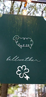 A green sign with a sheep outline, the word "bellwether," and a four-leaf clover with a key symbol below it.