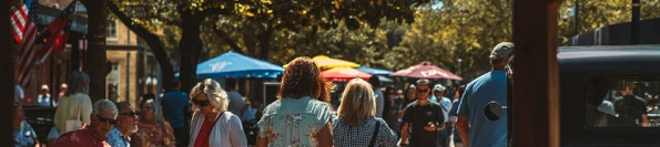 A sunny outdoor market with people strolling, a vendor row, umbrellas, and a vintage car as a clocked town square vibe.
