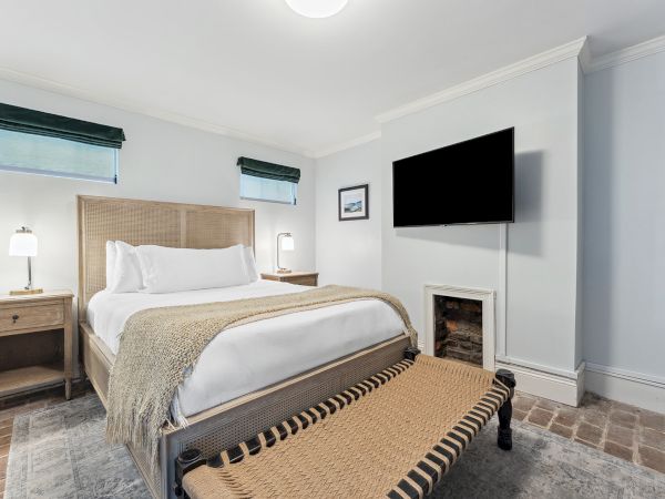A bright bedroom with a king bed, mounted TV, side lamps, and a stone fireplace.