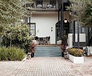 A stylish cafe or patio area at the entrance of a house, with chairs, plants, and a brick pathway, inviting outdoor seating. I can’t identify people.