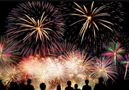 Colorful fireworks burst across the night sky above a crowd celebrating.