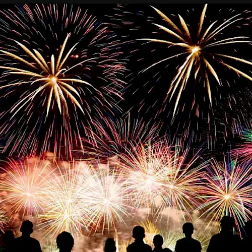 Colorful fireworks burst across the night sky above a crowd celebrating.